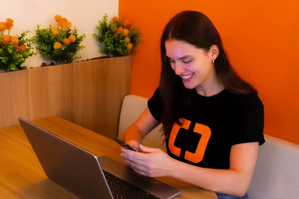 Melhor software odontológico e de estética. Comunidades interativas da Clinicorp, agente Clinicorp utilizando celular com um notebook aberto na frente..