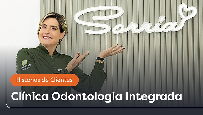Paperfree. Foto da Dra. Claudia Assis em sua clínica apontando para um arranjo na parede escrito 