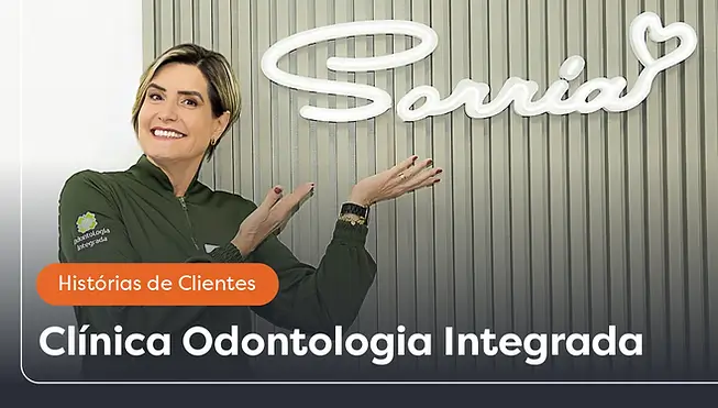 Paperfree. Foto da Dra. Claudia Assis em sua clínica apontando para um arranjo na parede escrito "Sorria".