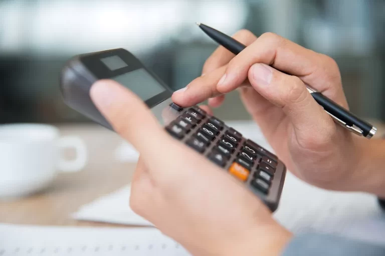 Custos fixos e variáveis: entenda o que são e a importância de um cálculo assertivo para sua clínica. Profissional de odontologia ou estética calculando os custos fixos e variáveis de sua clínica com uma calculadora na mão.