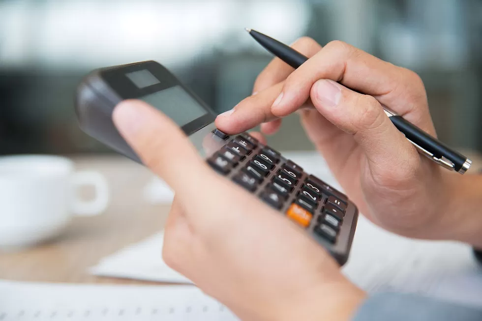 Custos fixos e variáveis: entenda o que são e a importância de um cálculo assertivo para sua clínica. Profissional de odontologia ou estética calculando os custos fixos e variáveis de sua clínica com uma calculadora na mão.
